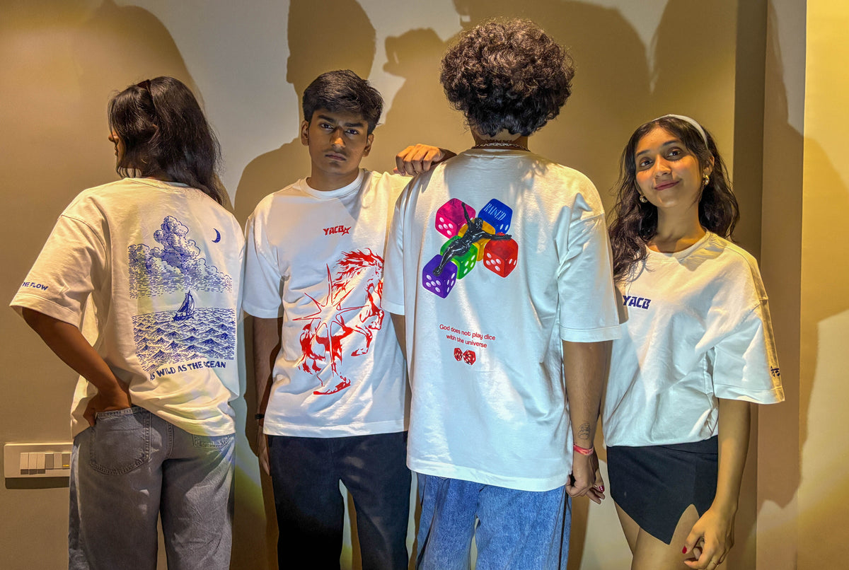 Four young people standing indoors, each wearing a white graphic T-shirt with different colorful back and front designs. The shirts feature large abstract and animal-style prints in red, blue, purple, green, and yellow.